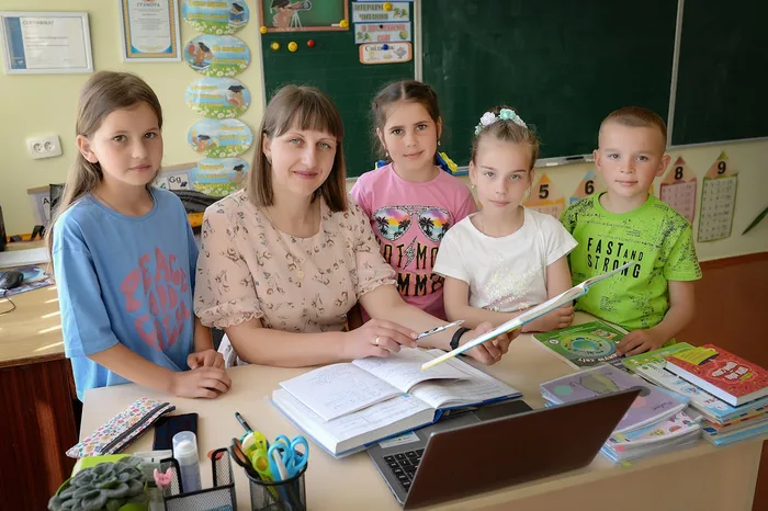 A teacher works one-on-one with a young student at a classroom desk.